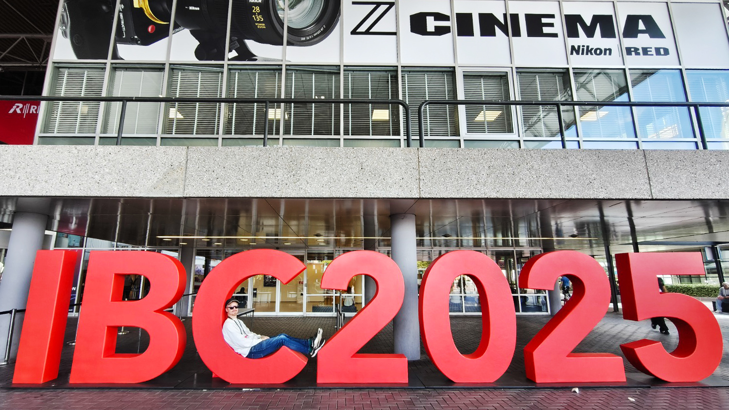 IBC 2025 attendee posing within the show's sign outside of the main entrance