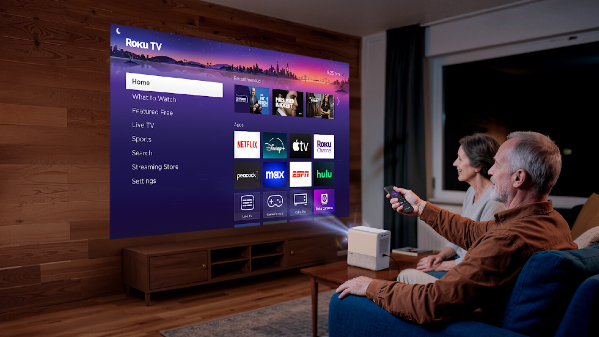 A middle-aged couple are very pleased with the Aurzen Roko TV Smart Projector, which is projecting the Roku TV interface onto a screen in their living room